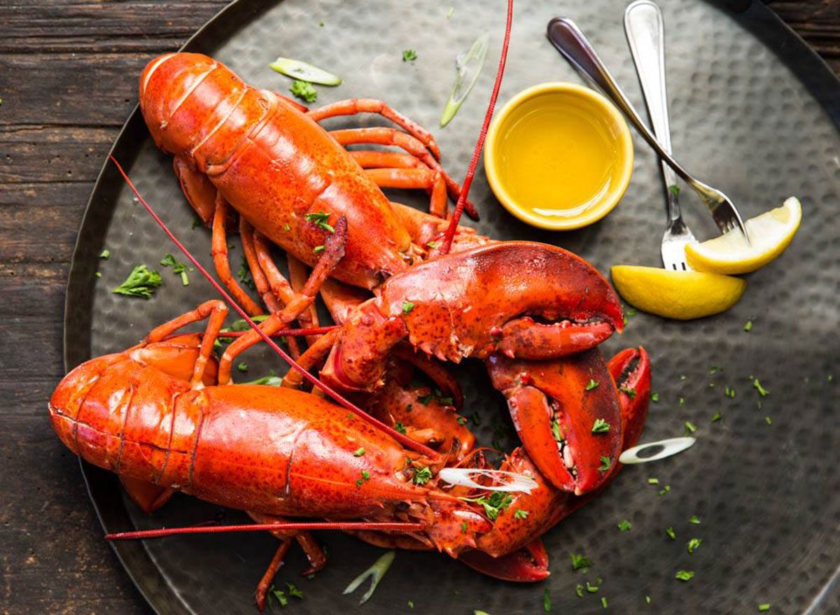 Two whole steamed lobsters on a platter with drawn butter and lemon wedges