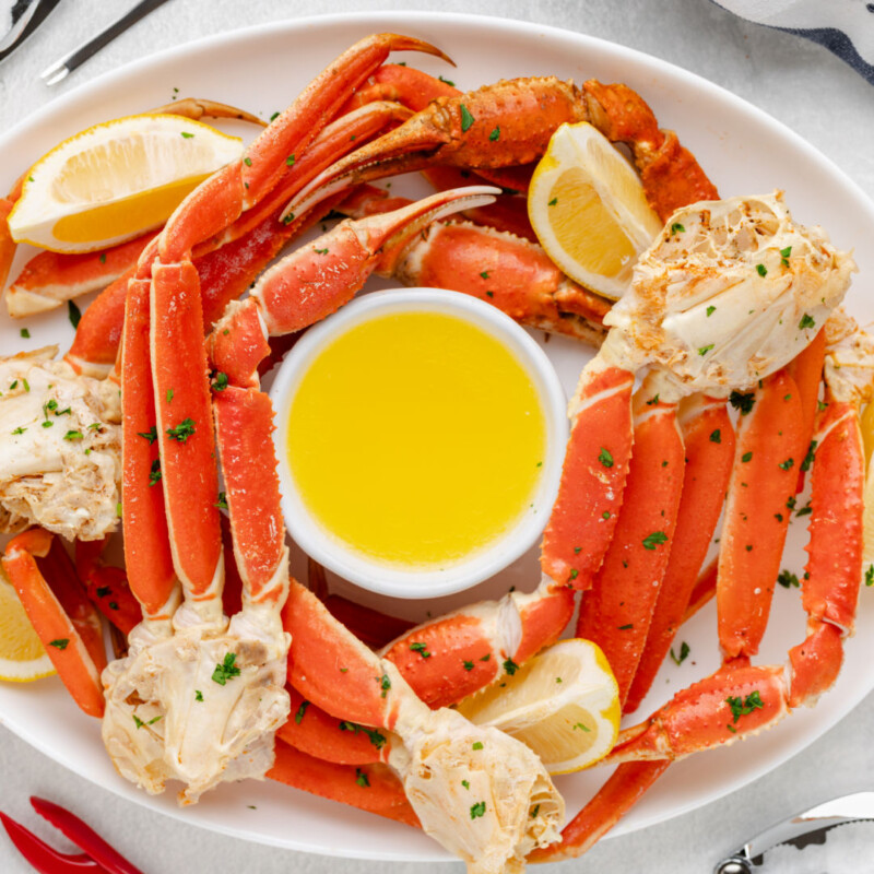Snow crab legs on a platter with drawn butter and lemon wedges